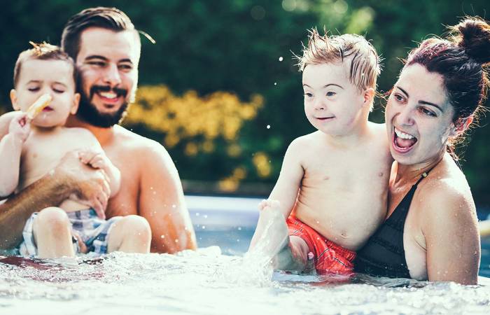 Little boy with Down syndrome eating popsicle in the swimming pool with his family