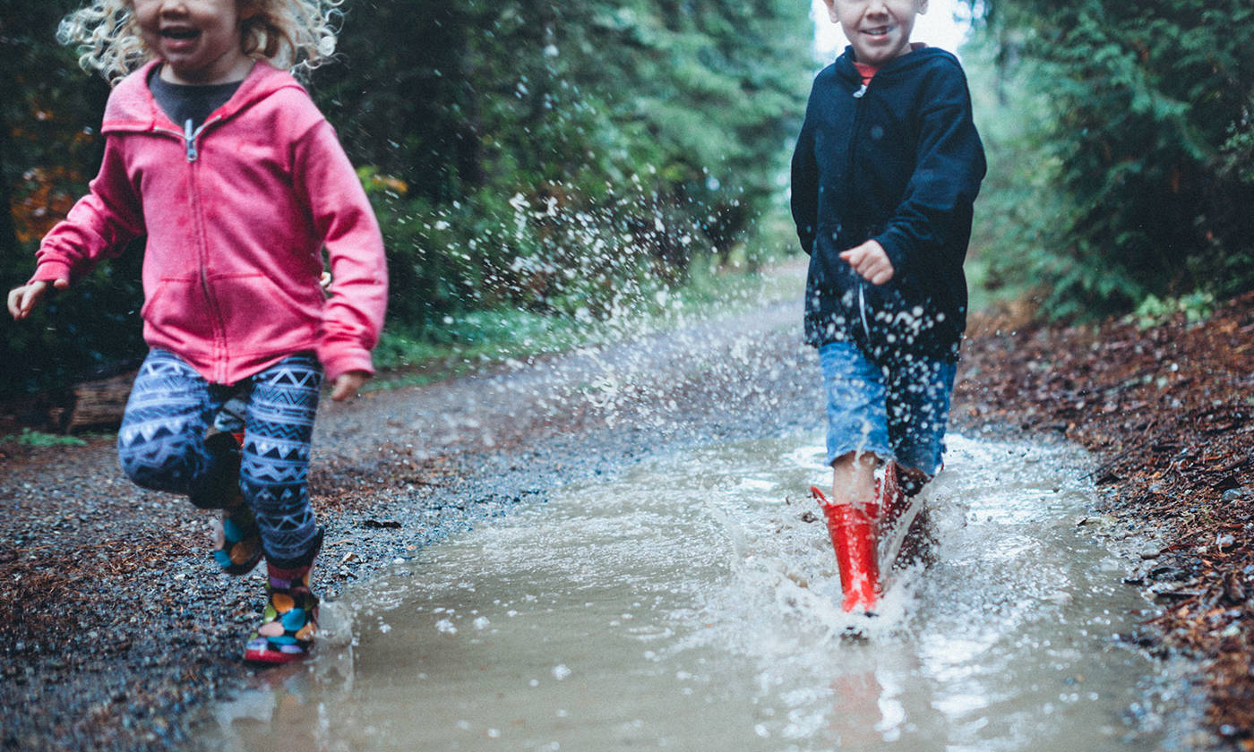 Children wearing rain boots splash and play in a mud puddle