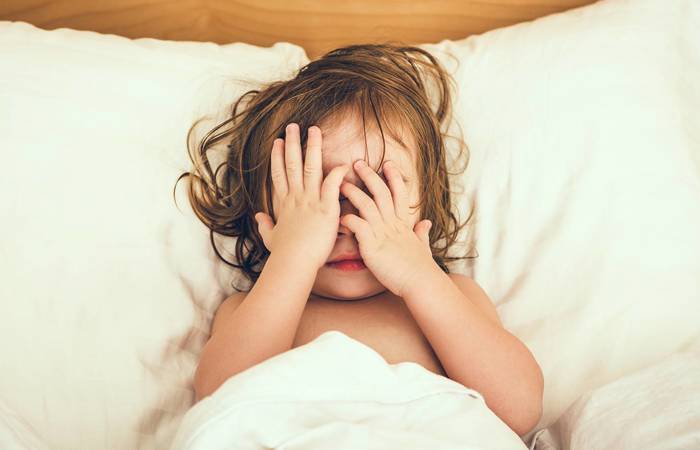 Little girl in bed covering her eyes