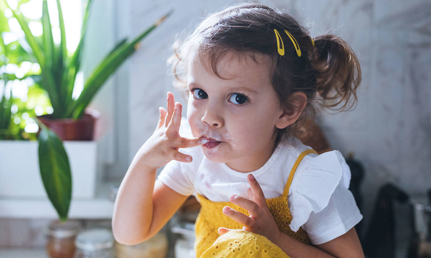 Little girl eating whipped cream with her fingers