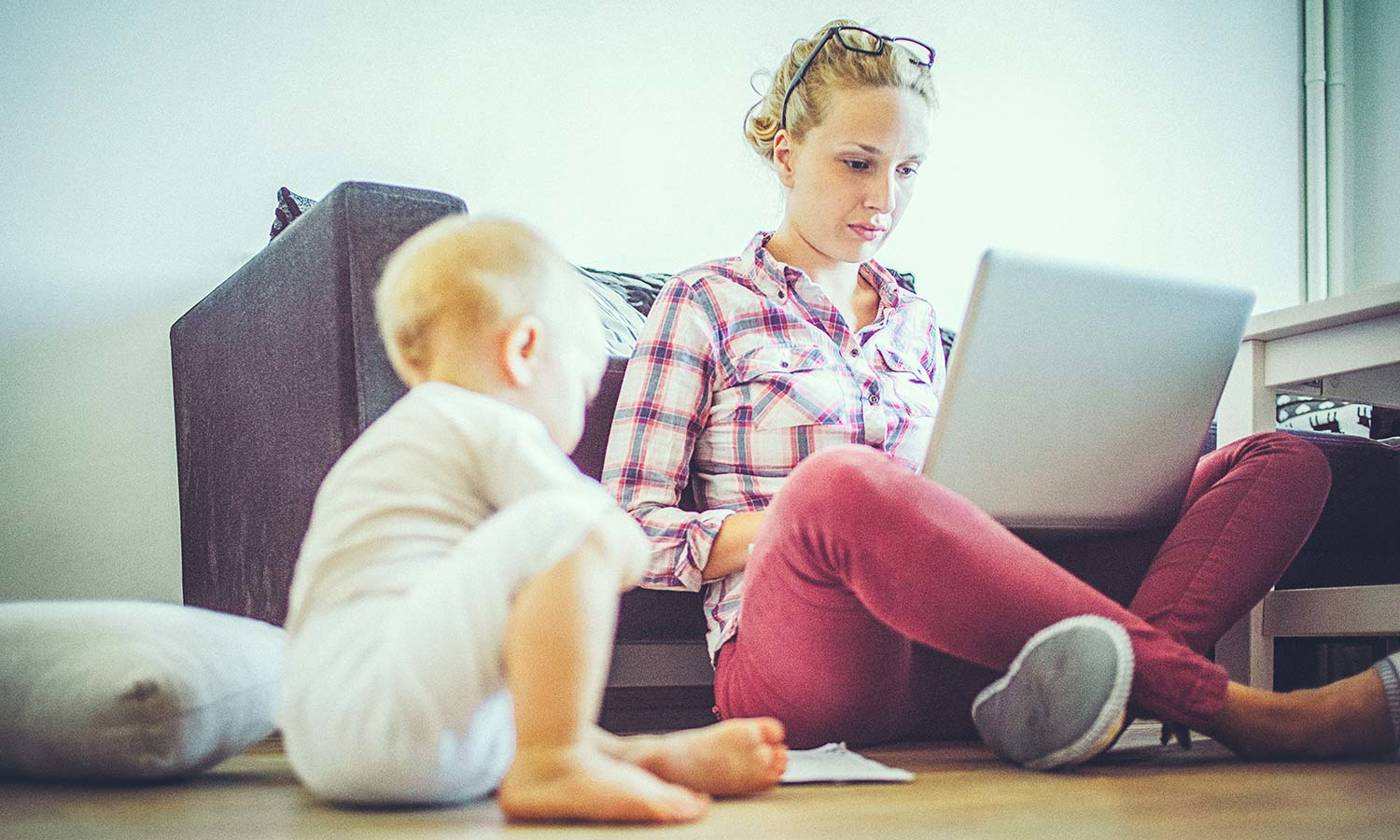 woman working on computer while baby plays