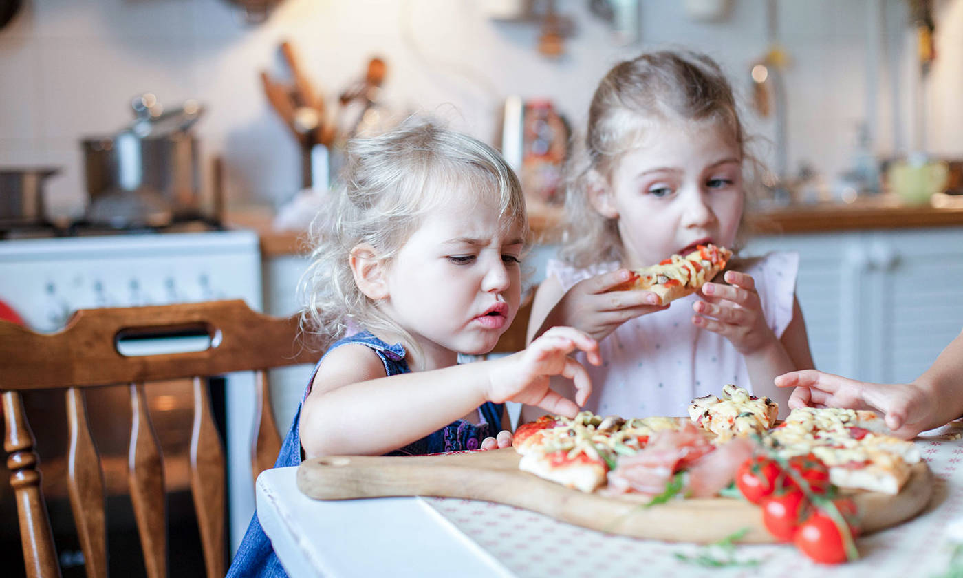 Children eating, tasting pizza in kitchen