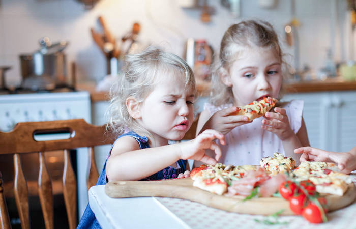 Children eating, tasting pizza in kitchen
