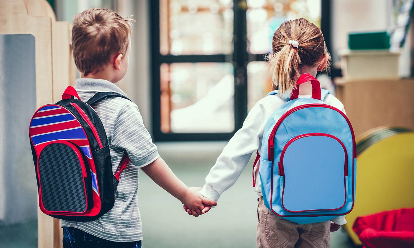 Small boy and girl holding hands walking into preschool