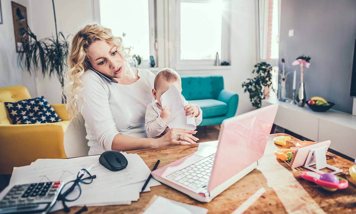 woman working on computer while holding baby