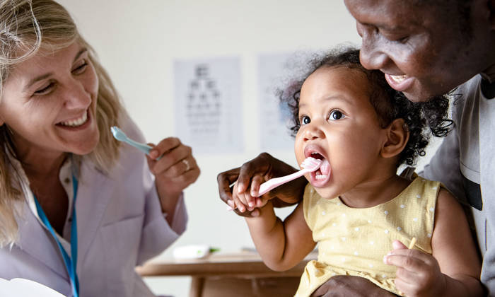 Dentist teaching a little girl how to brush her teeth