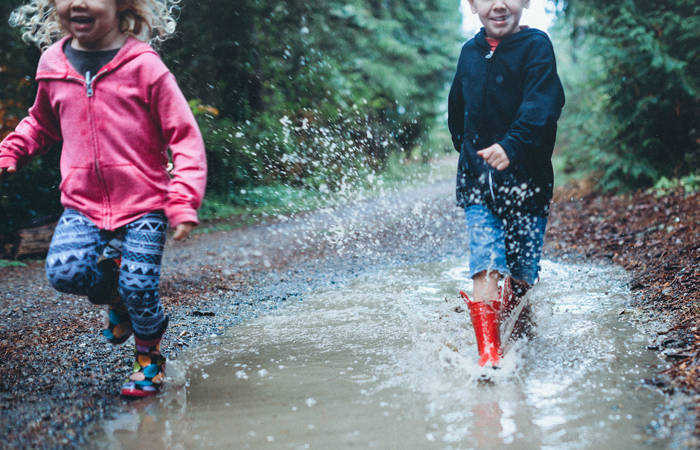 Children wearing rain boots splash and play in a mud puddle