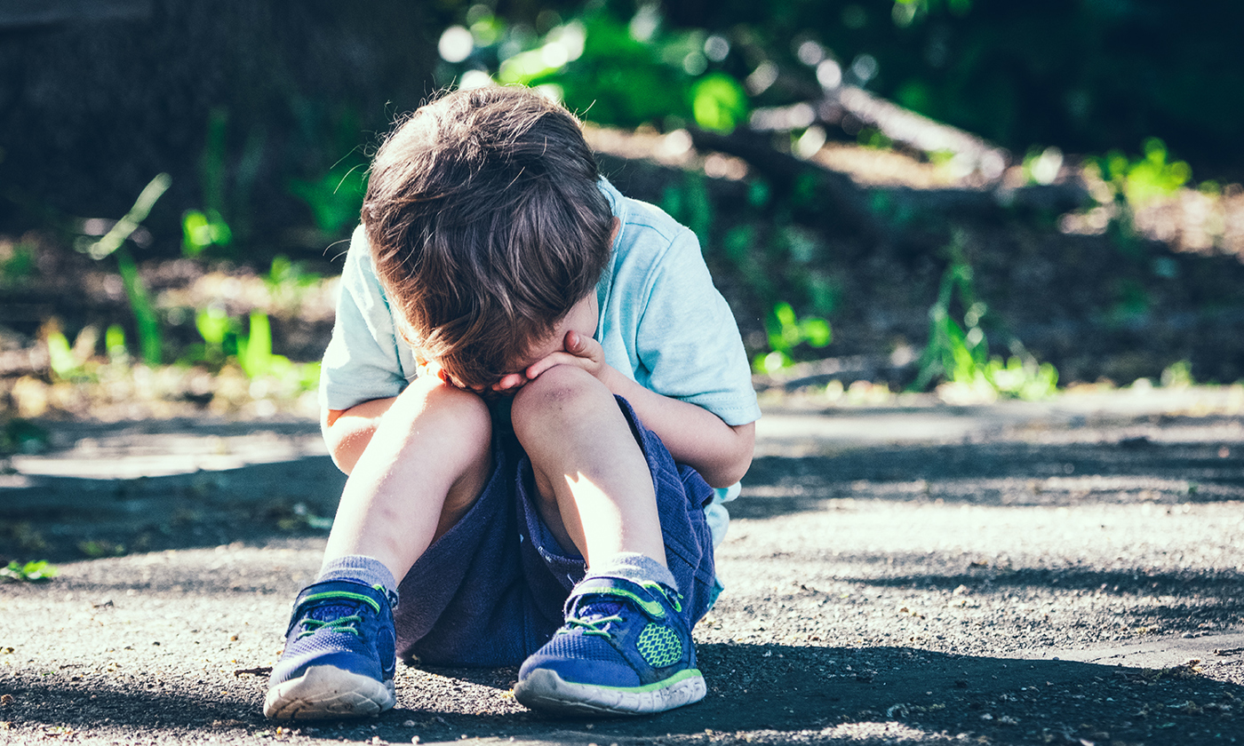 Crying toddler sitting on the floor covering his face