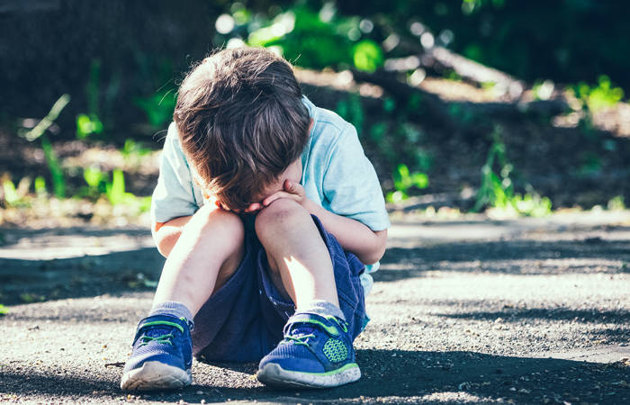 Crying toddler sitting on the floor covering his face