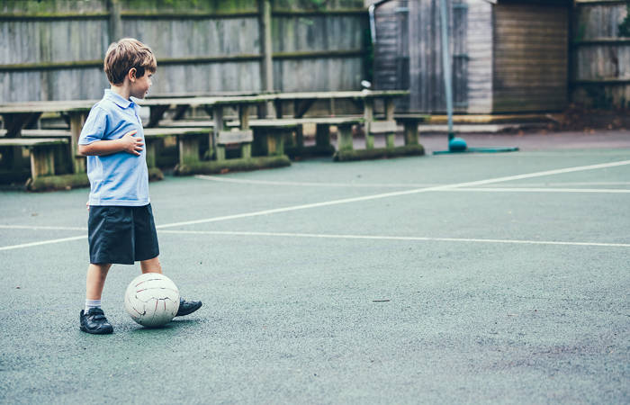 Boy in school uniform playing soccer alone in the school yard
