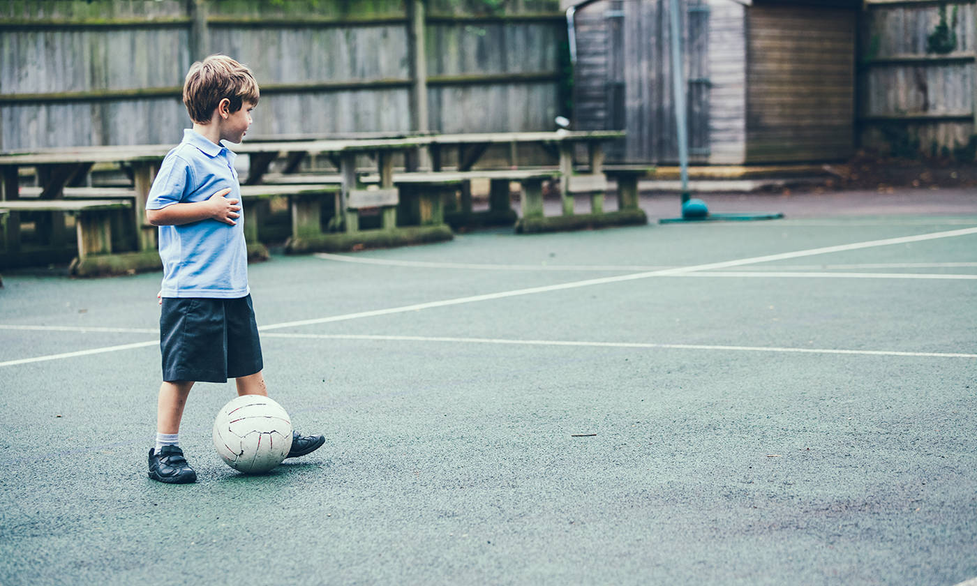 Boy in school uniform playing soccer alone in the school yard