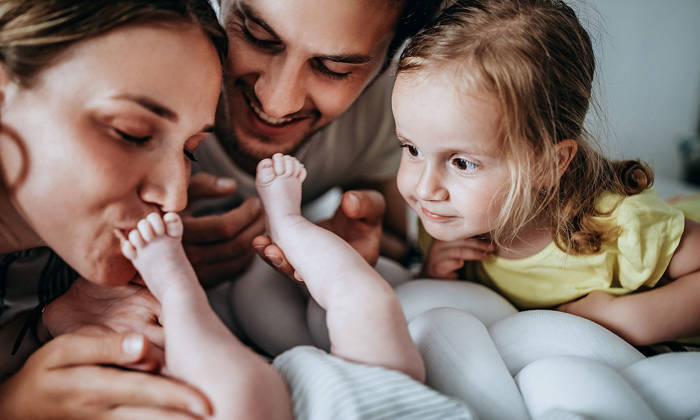 Family playing with new baby in bed
